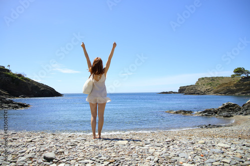 Happy tourist on the beach celebrating vacation raising arms