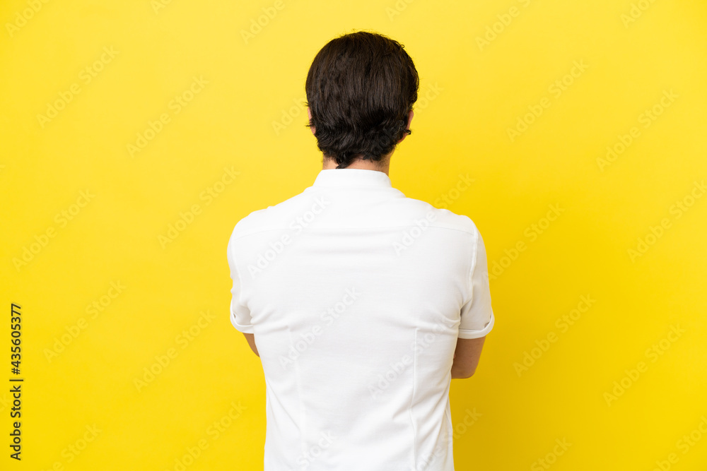 Young caucasian man isolated on yellow background in back position