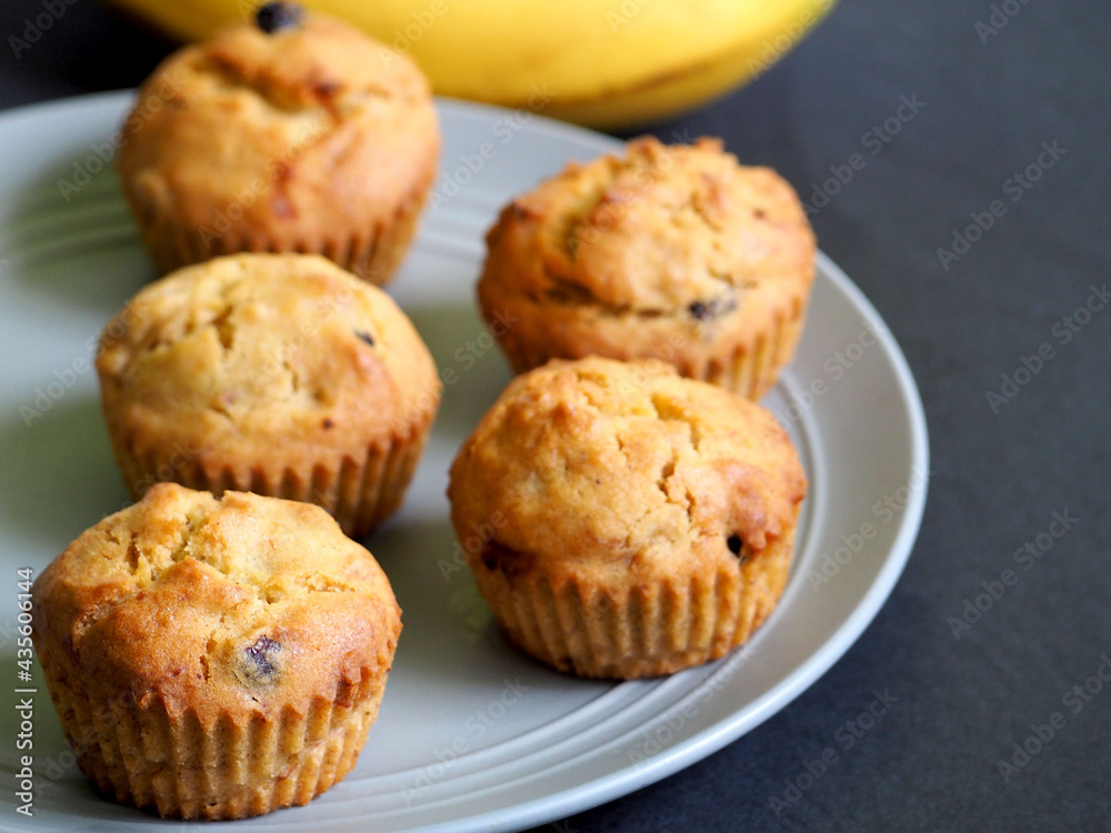 five vegan banana muffins with raisins gluten free stand on a gray plate against a black background, side view. homemade diet without lactose, eggs, gluten five vegan banana muffins with raisins gluten free stand on a gray plate against a black background, side view. homemade diet without lactose, eggs, gluten