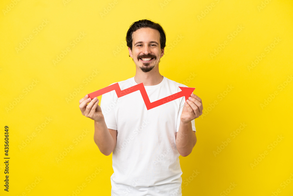 Young caucasian man isolated on yellow background holding a catching a rising arrow with happy expression Young caucasian man isolated on yellow background holding a catching a rising arrow with happy expression