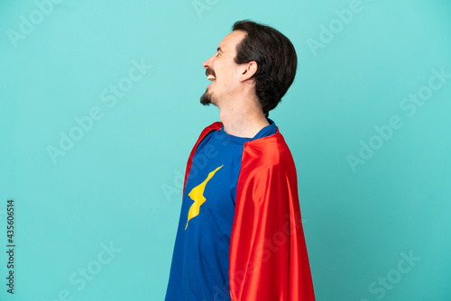 Super Hero caucasian man isolated on blue background laughing in lateral position