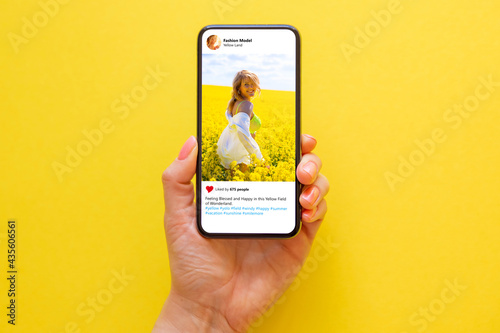 Mobile phone on yellow background with photo of woman in yellow meadow on the screen photo
