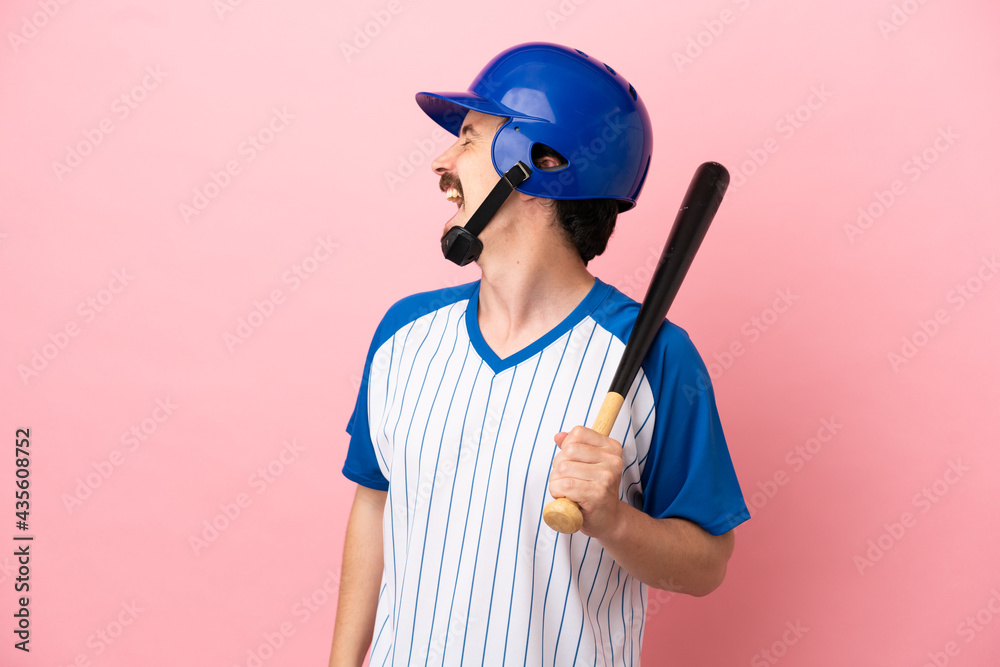 Young caucasian man playing baseball isolated on pink background laughing in lateral position Young caucasian man playing baseball isolated on pink background laughing in lateral position