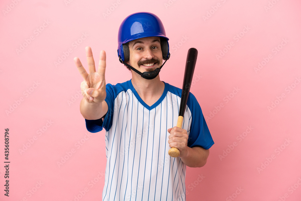 Young caucasian man playing baseball isolated on pink background happy and counting three with fingers