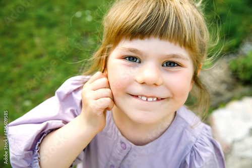 Portrait of happy smiling toddler girl outdoors. Little child with blond hairs looking and smiling at the camera. Happy healthy child enjoy outdoor activity and playing.