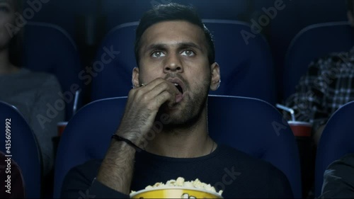 Man sitting in a movie theatre watching a movie, eating popcorn.