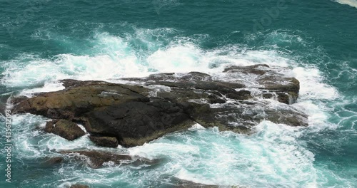 Ocean waves crashing stones and foaming on big rock at tropical beach with blue water.