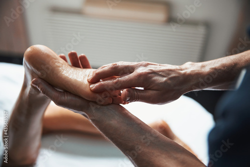 Unrecognized manual therapist doing massage on female feet in spa salon