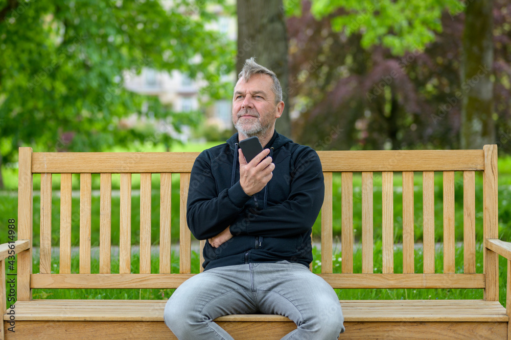 Obraz premium Middle-aged man relaxing on a park bench with his mobile