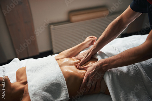 Young beautiful woman under the towel relaxing stomach massage at spa salon
