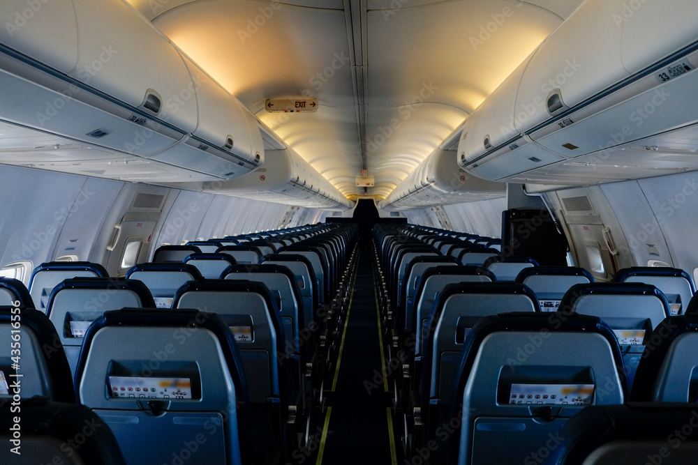 Fototapeta premium Rows of black leather seats and porthole windows in commercial aircraft cabin. Economy class chairs of airplane. Background, copy space, close up.