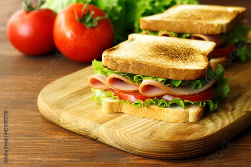 sandwich with ham, green lettuce and tomato on a wooden brown kitchen board