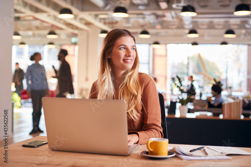 Young Businesswoman Sitting At Desk Working On Laptop In Modern Open Plan Office