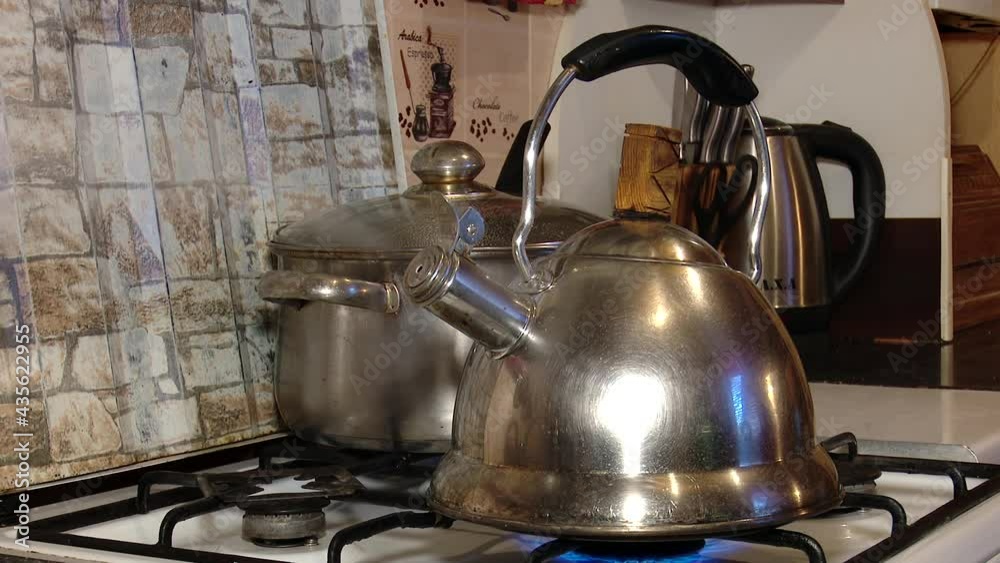 a metal kettle with a whistle stands on a gas stove against the background of other kitchen appliances the kettle is boiling a metal kettle with a whistle stands on a gas stove against the background of other kitchen appliances the kettle is boiling