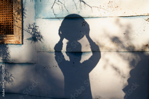 The shadow of a teenage boy holds a large round ball over his head