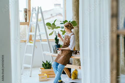 Canvas Print Blond inspired woman gardener in apron replant potted houseplant in greenhouse or home interior
