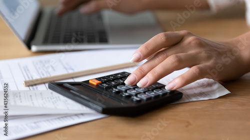 Close up young woman using calculator, managing household budget, counting paper bills or taxes, managing monthly budget, doing financial paperwork alone at home, accounting bookkeeping concept.