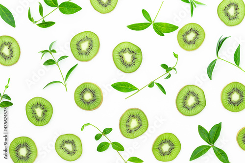 Summer bright background with slices of kiwi and green leaves on the gray surface