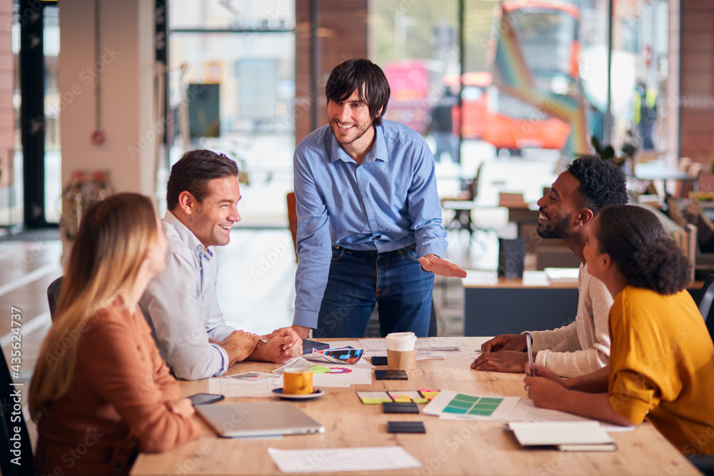 Fototapeta premium Businessman Giving Presentation To Colleagues Sitting Around Table In Modern Open Plan Office