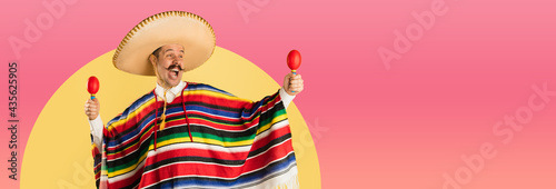 Happy man in sombrero and bright poncho isolated over red yellow background