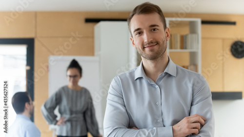 Head shot portrait of confident businessman executive owner standing in office with arms crossed, successful young man employee intern worker looking at camera, posing for corporate photo alone