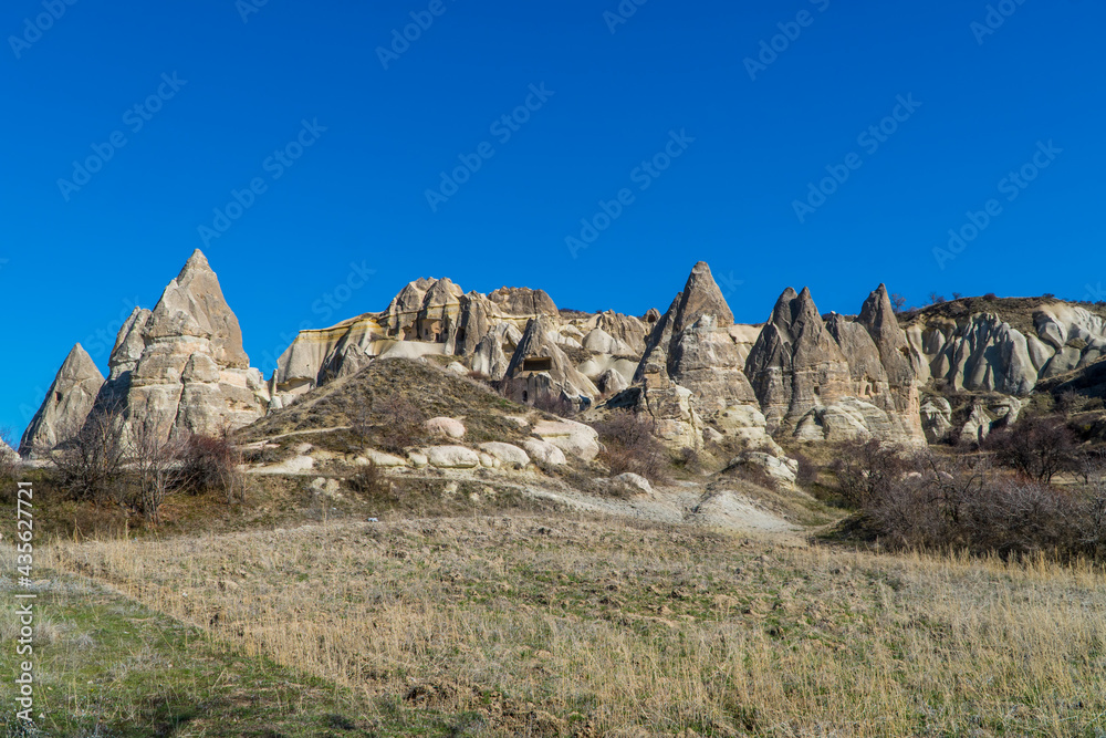 Beautiful panorama view of a field and caves inside typical rock formations and fairy chimneys in Cappadocia, Turkey