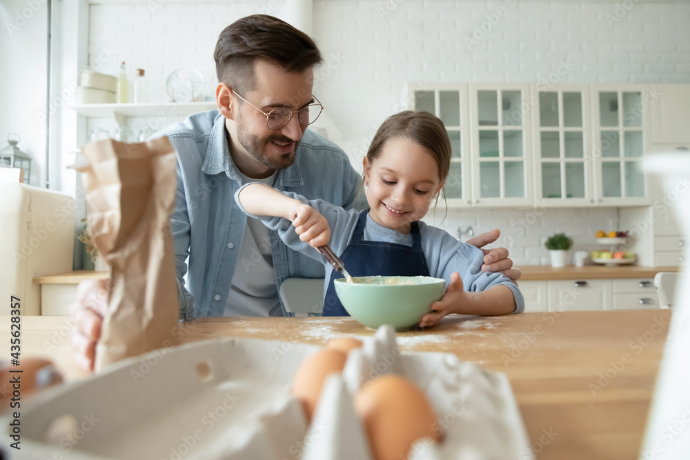 Happy loving young Caucasian father and little daughter mix flour bake cookies or pie together in kitchen. Smiling caring dad and small girl child have fun prepare dessert food. Parenthood concept. Happy loving young Caucasian father and little daughter mix flour bake cookies or pie together in kitchen. Smiling caring dad and small girl child have fun prepare dessert food. Parenthood concept.