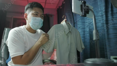 Entrepreneur of Asian young man live streaming video online for selling her dress and clothes to the customer in platform or application online, a hobby concept during a COVID-19 quarantine period.