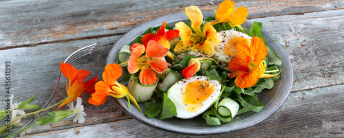 plate of salad with cucumbers, eggs and edible nasturtium flowers on a wooden table, space for text