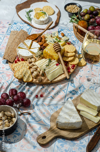 Cheese plate with variety of appetizers on table. Fresh brie cheese and camembert cheese whith crackers, pears, grapes, olives, rosemary, orange jam, orange jam, nuts, honeycomb and wine.
