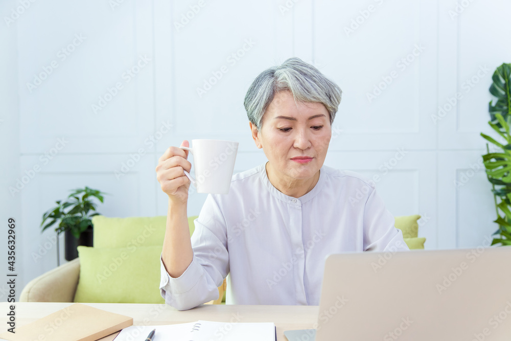 Senior Asia business woman is holding a cup of coffee while working from home