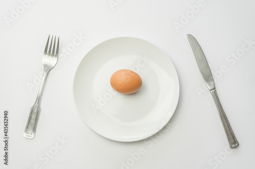 Dish with one raw egg fork and knife isolated on white background.Top view minimal food concept.