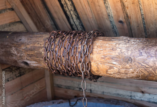 Metal chain in a wooden well for lifting a bucket of water, close-up. Traditional photo