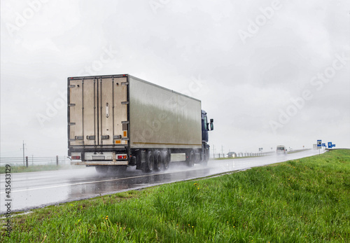 A trucker on a truck with a semitrailer transports cargo in poor visibility on the road, rain. Highway traffic in bad weather. Copy space for text