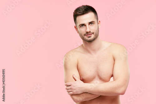 Portrait of handsome confident muscular man with crossed arms and naked torso looking in camera on pink background