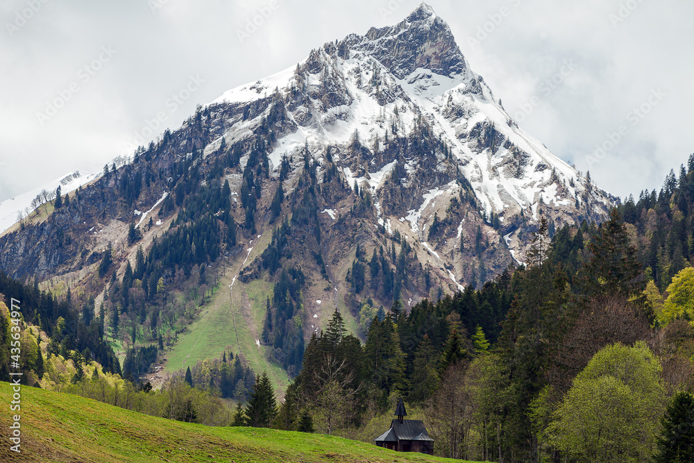 Wilde Bergnebel in den Allgäuer Alpen mit verschneiten Gipfeln und frischem Grün im Tal