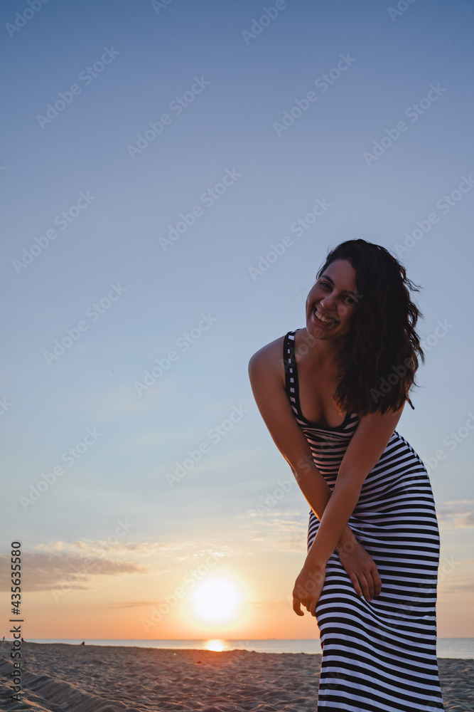 Obraz premium young beautiful sexy woman in dress walking bay sandy beach at sunset