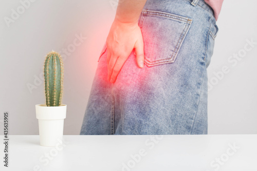 A cactus in the foreground, in the background a girl in a skirt is holding her anus with her hand. Hemora and proctitis diseases concept, proctology and muscle syndrome photo
