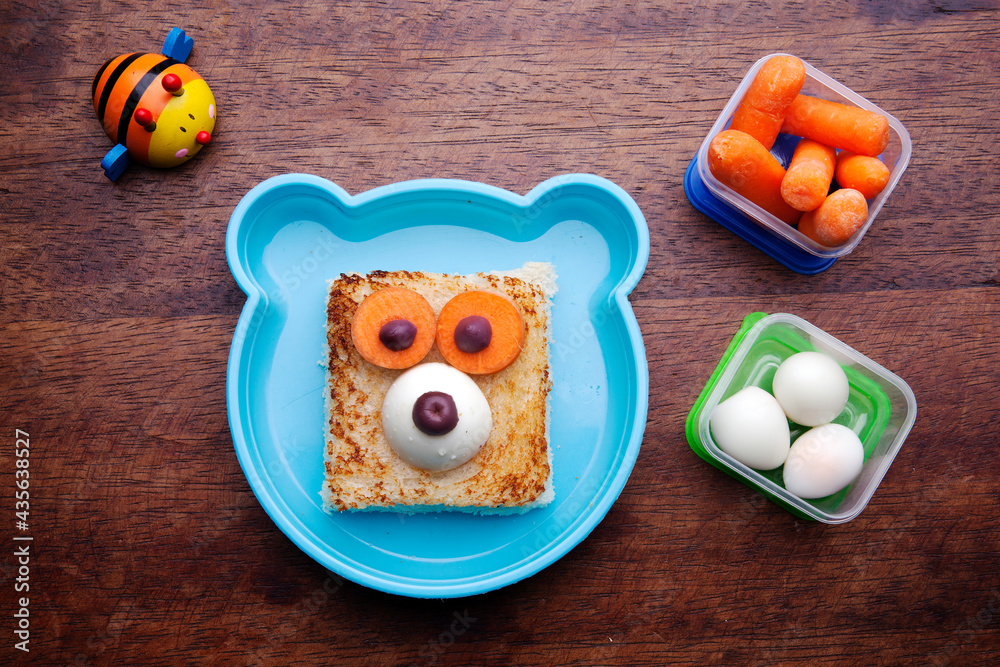 Obraz premium School lunch box snacks for kids over wooden background. Back to school. Healthy and fun snack option for moms. Cute food art creative concepts. Bow with fruits and vegetables and cute sandwich.