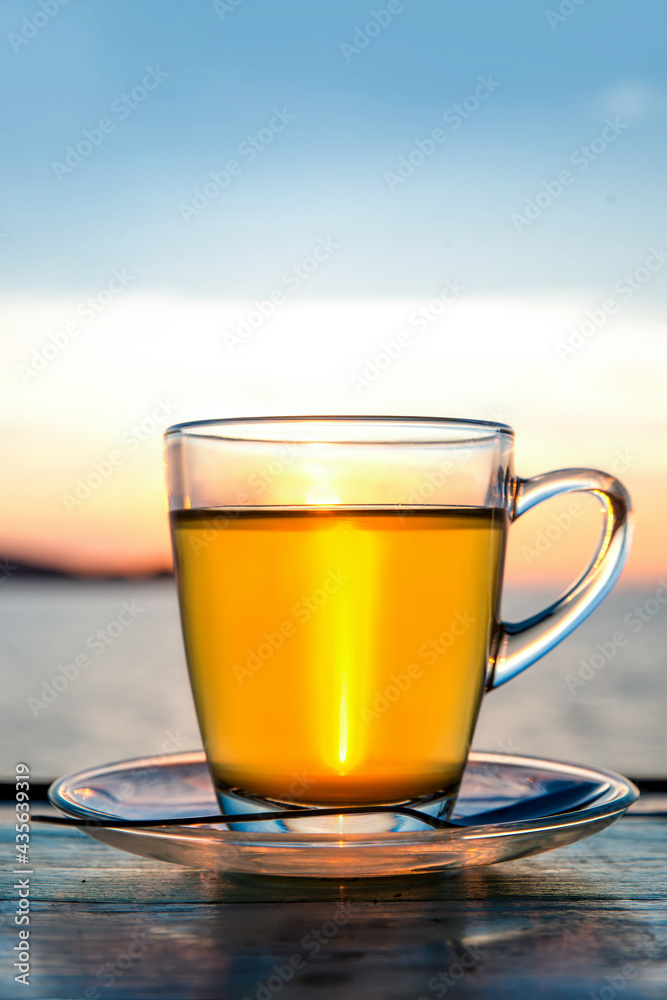 Cup of green tea front of at sunset light on wooden tabletop.