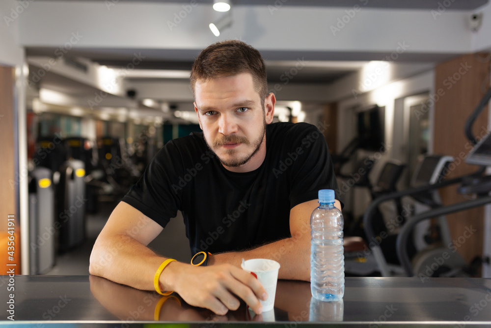 man with drinking water while resting in a generic out of focus fitness club. man with drinking water while resting in a generic out of focus fitness club.