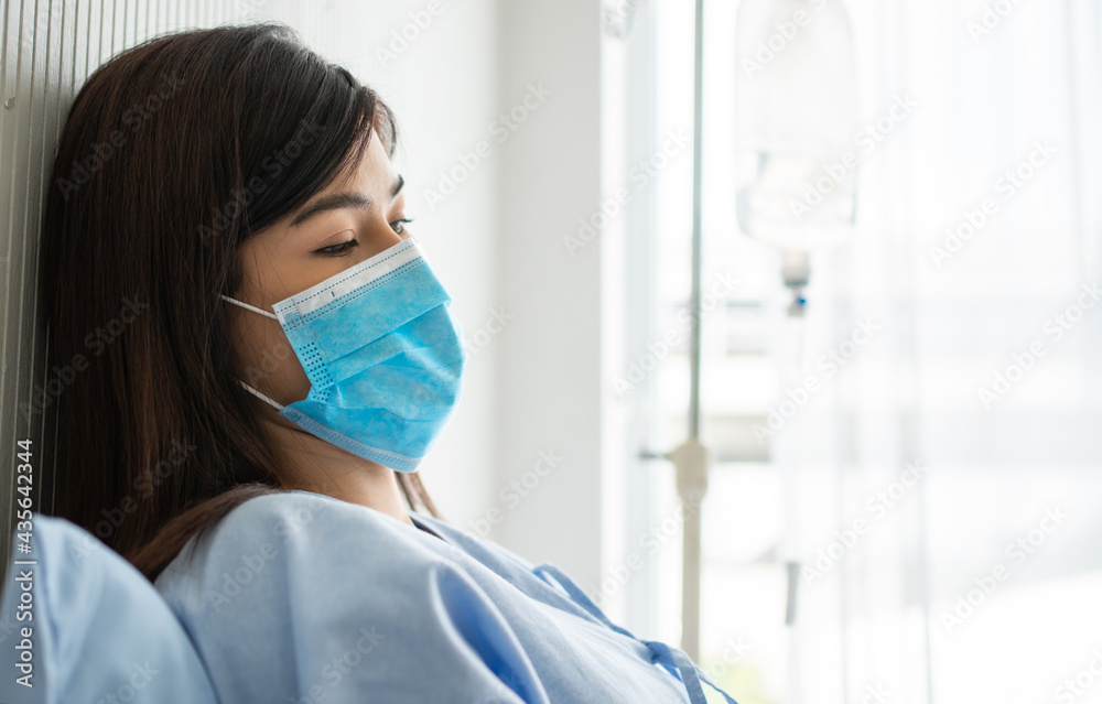 Sad Asian patient woman lying on the hospital bed and wearing a face mask to protect coronavirus. Concept of Health care, quarantine coronavirus (COVID-19), and Health insurance. Sad Asian patient woman lying on the hospital bed and wearing a face mask to protect coronavirus. Concept of Health care, quarantine coronavirus (COVID-19), and Health insurance.