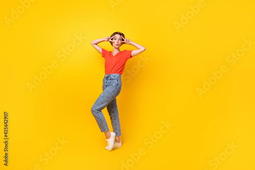 Full body portrait of nice young girl two hands fingers show v-sign near eyes isolated on yellow color background