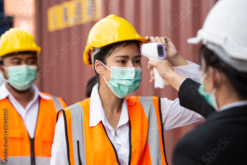 Female worker scanning fever temperature with digital thermometer to construction site staff wearing hygiene face mask protect from Coronavirus or COVID-19. New Normal working