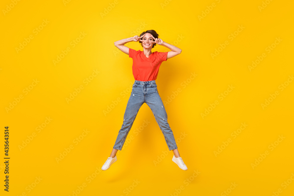 Full body photo of cheerful charming girl fingers show v-sign near eyes toothy smile isolated on yellow color background