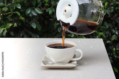 Canvas Print pouring coffee into cup on the table in the garden scenery