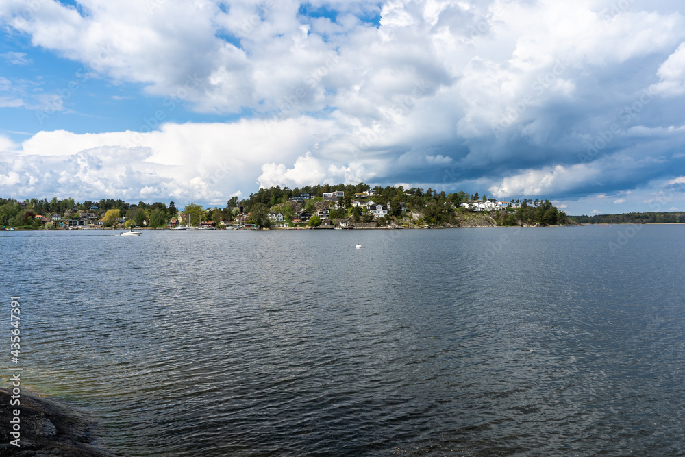 Amazing Panorama of the Baltic Sea Bay on sunny spring day. Rocky shores of Scandinavia covered with evergreen forests. Traditional Swedish wooden villas houses on the coast. Blue sky white clouds.