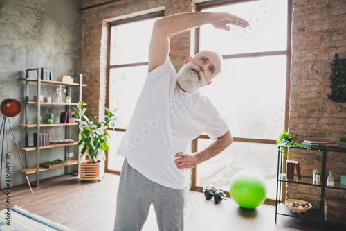 Photo of sportive focused concentrated mature man grandfather stretcing spine training muscles at home house photo