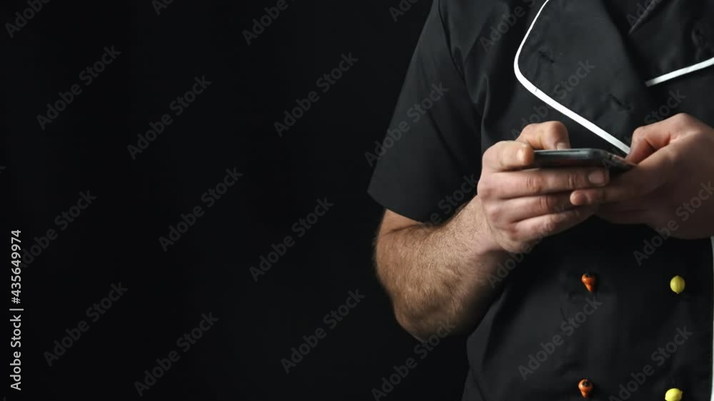 Torso of a man in a black apron using a smartphone,black background.