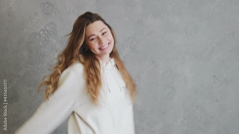 The laughing woman in hoodie dancing in a gray studio The laughing woman in hoodie dancing in a gray studio